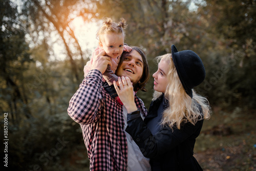 Happy smiling family is walking autumn in the park. A 6 month old baby girl is sitting on her father's shoulders and playing with her mother in the fall park.