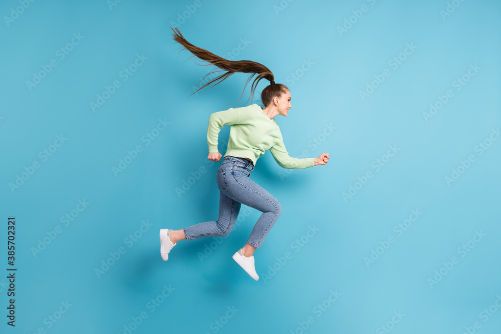 Full length body size side profile photo of jumping running hurrying girl with long hair ponytail isolated on bright blue color background Full length body size side profile photo of jumping running hurrying girl with long hair ponytail isolated on bright blue color background