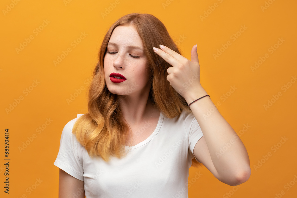 Serious girl with wavy redhead, pointing hand and fingers to head like gun, suicide gesture Serious girl with wavy redhead, pointing hand and fingers to head like gun, suicide gesture