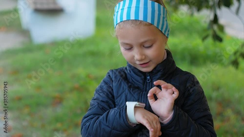 Child using smartwatch outdoor in autumn park. Kid talking on vdeo call on the smartphone. Schoolgirl using touchscreen display on watches browsing internet. Smart kids wristwatch with GPS tracker.