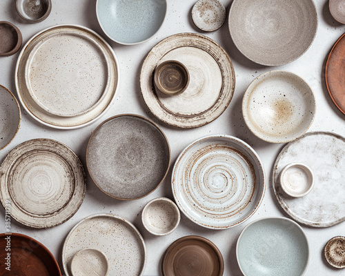 Fototapeta handmade ceramics, empty craft ceramic plates and bowls on light background, top