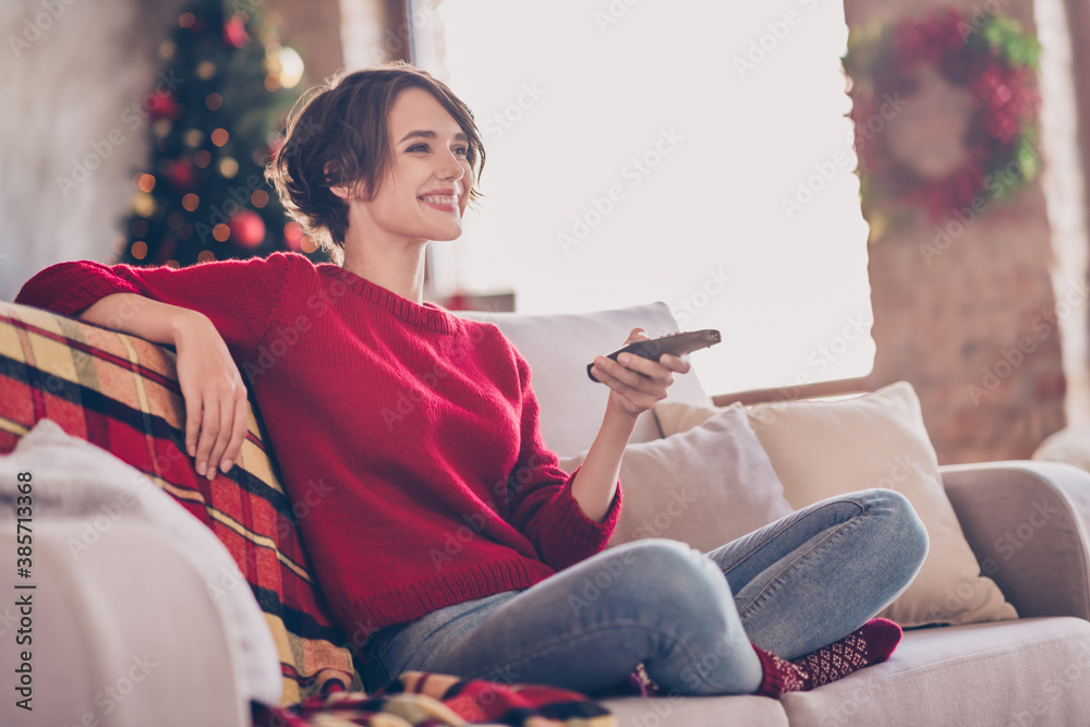 Photo of lovely young lady hold remote control sitting sofa toothy smile wear red pullover jeans socks indoors - obrazy, fototapety, plakaty 