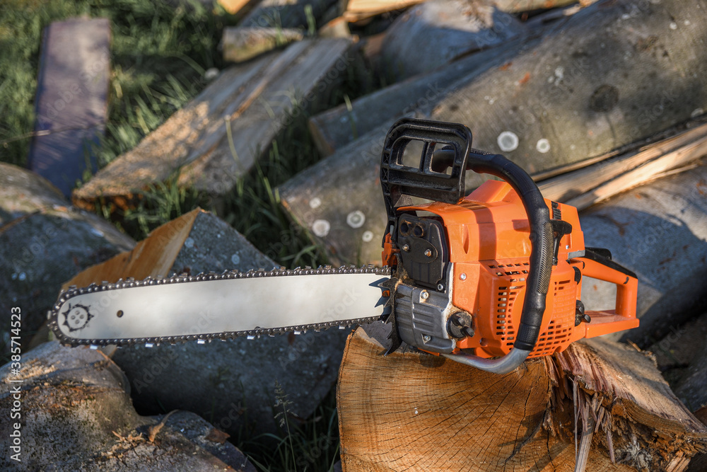 Chainsaw that stands on a heap of firewood in the yard on a background of firewood and trees cut by a chainsaw