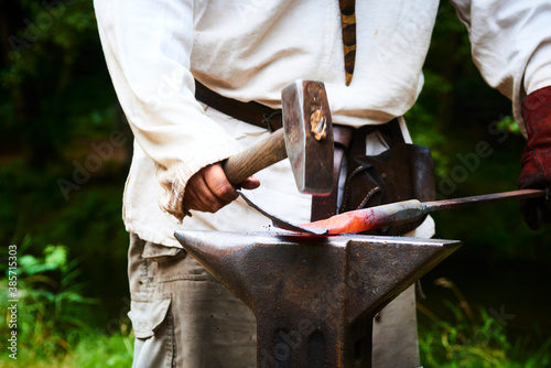 The blacksmith manually forging the molten metal on the anvil in smithy with spark fireworks 