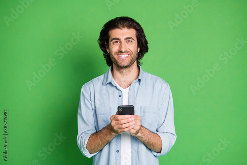 Photo of man hold telephone look camera toothy smile wear denim shirt isolated green color background