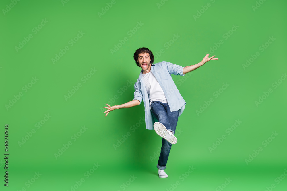 Full length photo of bristled guy funny open mouth leg you wear denim shirt jeans sneakers isolated green color background