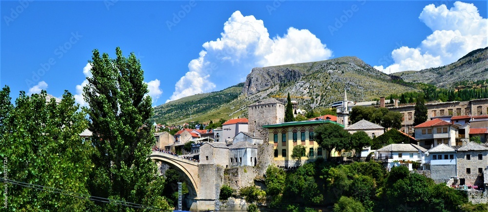 Obraz premium City of Mostar Bosnia and Hercegovina.Ancient and Ottoman City of Mostar and great Mostar Bridge. Neretva River and Vintage Buildings during sunny day and blue sky.