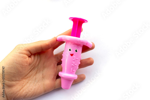 Hand holds toy baby pink syringe on white background.