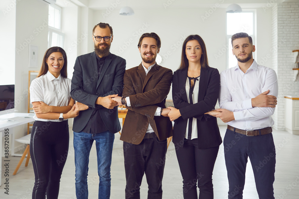 Young office workers or startuppers standing together holding hands looking at camera Young office workers or startuppers standing together holding hands looking at camera
