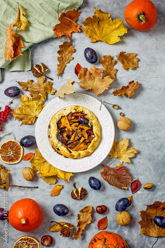 Autumn pie with plums and pumpkin on a light plate surrounded by fallen leaves, acorns, plums, linen napkins. Autumn still life with homemade cakes. Thanksgiving pie Top view, flat lay