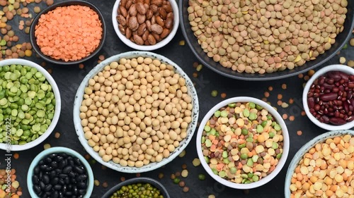 Legumes, lentils, chickpeas and beans assortment in various bowls on black stone background, top view