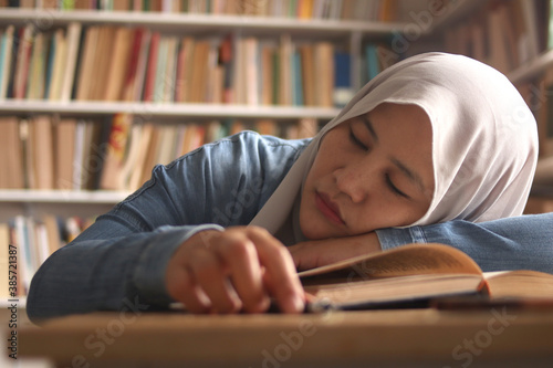 Asian muslim female student, studying hard in library, reading books, preparing for exam, tired exhausted expression
