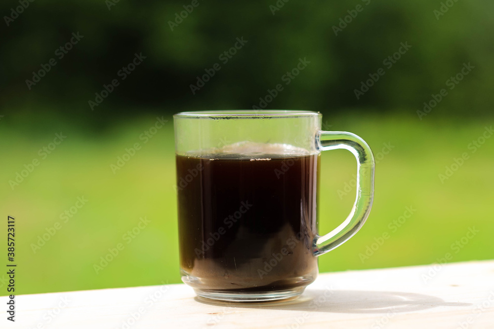 A glass transparent cup with black coffee, from which steam is rising. A glass transparent cup with black coffee, from which steam is rising.