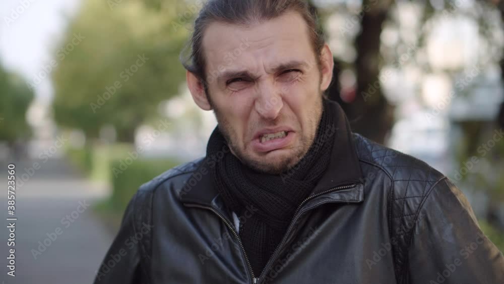 Young man in black jacket expressing disgust and disapproval with negative facial expressions outdoors. Young man in black jacket expressing disgust and disapproval with negative facial expressions outdoors.
