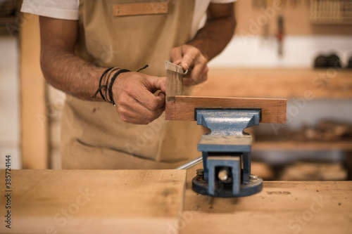 Close up of a young man working as carpenter in small carpentry workshop. View of a wood worker cutting a piece of timber with a hand saw. Young entrepreneur concept lifestyle.