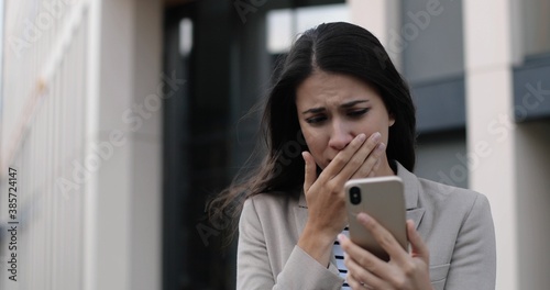 Close up portrait of beautiful unwell Caucasian woman standing in city and coughing while tapping on smartphone. Sick young female worker outdoors having cold and texting on cellphone. Virus concept