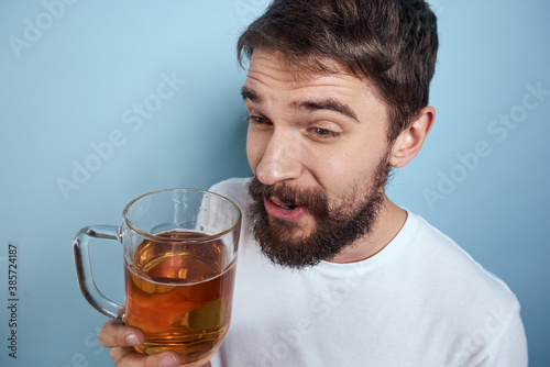 Cheerful man in a white T-shirt with a beer mug drunk blue background