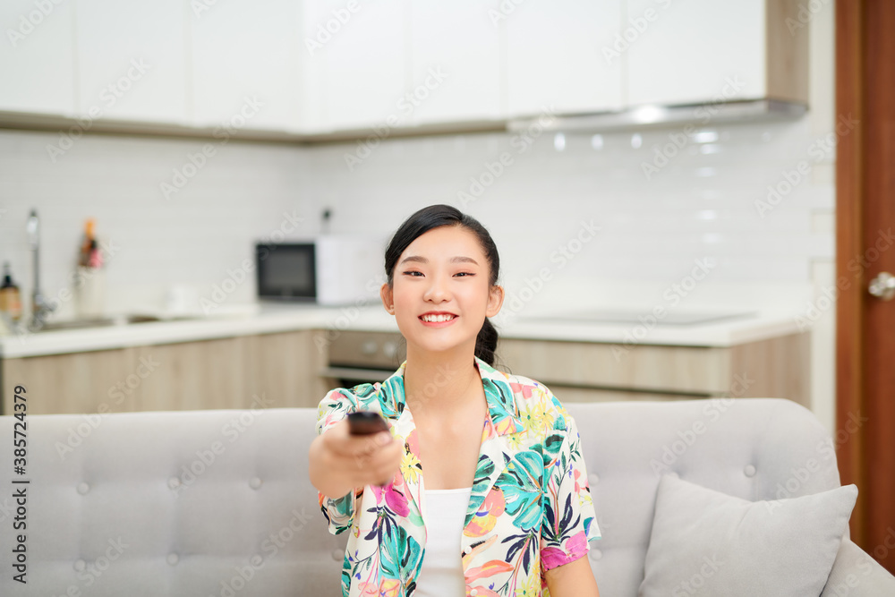 Smiling asian woman on couch changing tv channel at home in the living room Smiling asian woman on couch changing tv channel at home in the living room