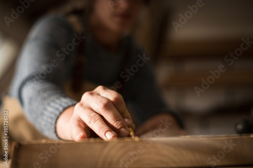 A young female carpenter working as wood designer in a small carpentry workshop. Young business woman handcrafting a piece of timber and designing new house furniture. Entrepreneurs concept lifestyle © Martina