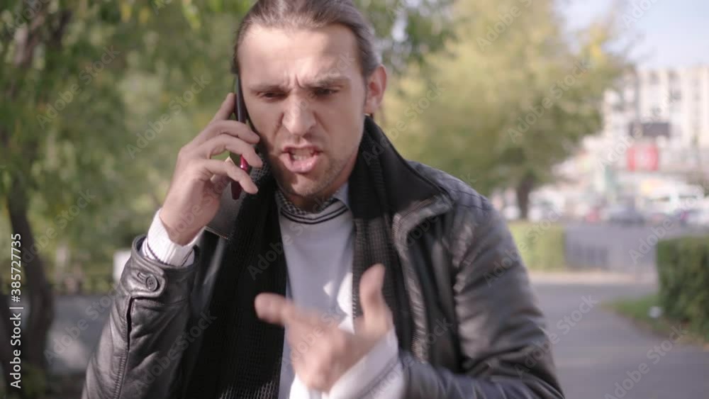 Rough emotional talking on a cell phone. Negative emotions. Upset man talking on a smartphone on a city street. Concept of people and emotions. Rough emotional talking on a cell phone. Negative emotions. Upset man talking on a smartphone on a city street. Concept of people and emotions.