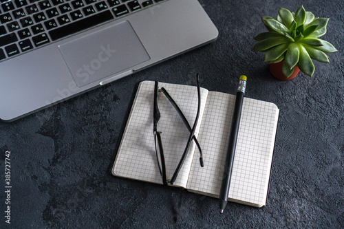 on the table is an open notebook, a pencil and glasses. There is a laptop nearby