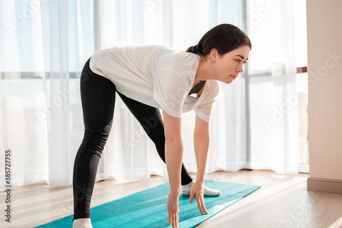 Yoga in the room. A young pretty woman trains at home on a sports mat, and leans forward. The concept of home workouts