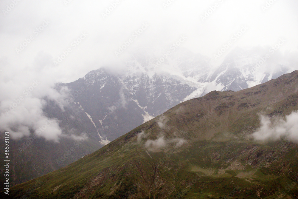 Fototapeta premium Peaks and slopes of mountains in foggy weather. Elbrus region near the village of Terskol. Caucasus, Russia.