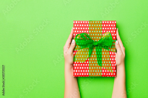 Top view of female hands holding christmas or other holiday handmade present box package in the palms, flat lay table background with copy space