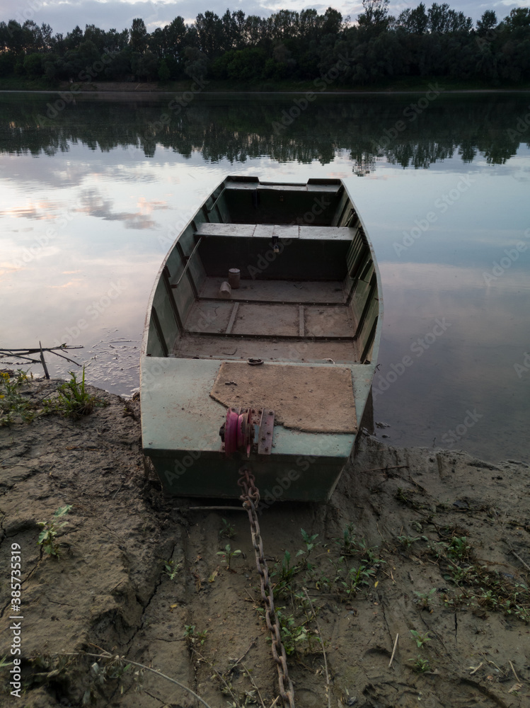 An old fishing boat moored along the muddy bank of the Sava River in Bosanski Brod during the summer evening An old fishing boat moored along the muddy bank of the Sava River in Bosanski Brod during the summer evening