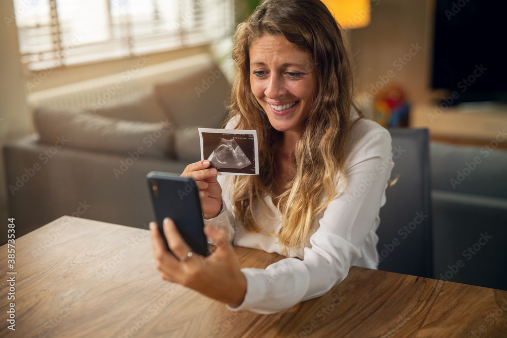 Authentic slow motion close up shot of an young pregnant woman is making a video call to her relatives or friends and showing an ultrasound to announce her future child birth.