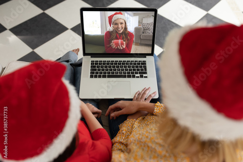 Woman and daughter in Santa hats having a video chat with another woman on her laptop at home
