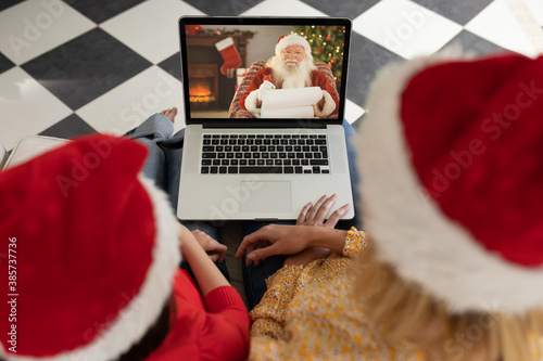 Woman and daughter in Santa hats having a video chat with Santa Claus on her laptop at home