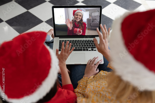 Woman and daughter in Santa hats having a video chat with another woman on laptop at home