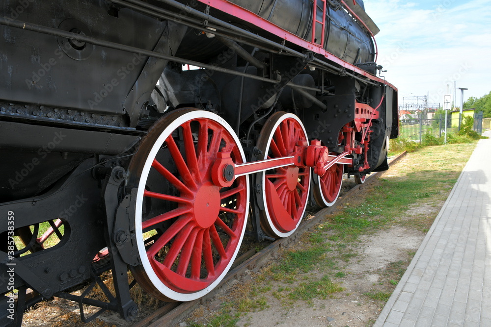 Close up on a set of red and white wheels of an old black and red train standing on a side track seen on a sunny summer day in Poland next to an abandoned train station 