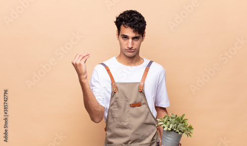 young gardener man making capice or money gesture, telling you to pay your debts!