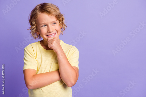 Photo of minded kid touch fingers face look empty space think thoughts wear yellow t-shirt isolated over purple color background