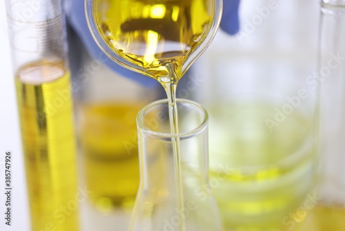 Scientist's hand in rubber glove pours yellow liquid into glass test tube in chemical laboratory closeup. Drug production pharmaceutical technology concept.