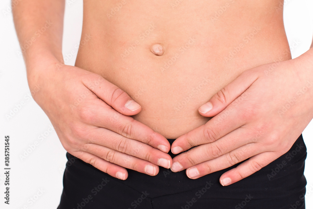 Young spotr girl suffering from stomach ache isolated on white background. Close up female person body in sportswear with pain in stomach. Young spotr girl suffering from stomach ache isolated on white background. Close up female person body in sportswear with pain in stomach.