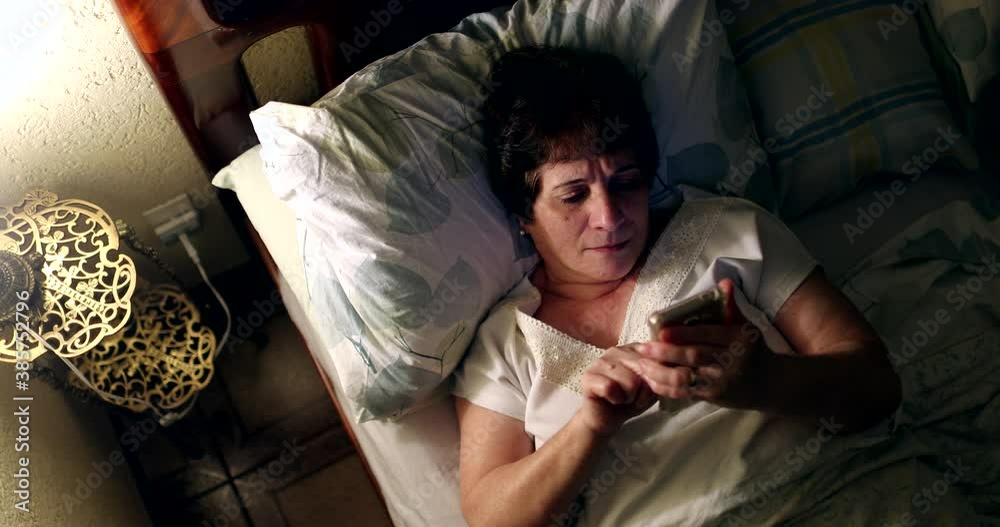 Woman laying in bed looking at cellphone screen, top view Woman laying in bed looking at cellphone screen, top view