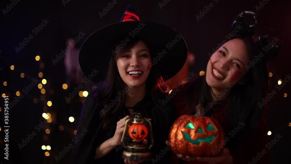 An asian woman wearing a witch costume holds an orange pumpkin. Young women were at the Halloween party. Two girl are having fun at the Halloween party. An asian woman wearing a witch costume holds an orange pumpkin. Young women were at the Halloween party. Two girl are having fun at the Halloween party.