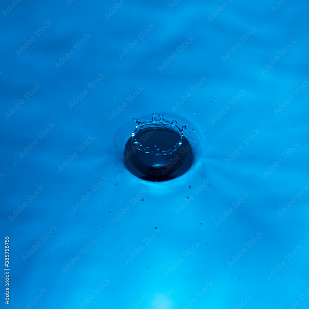 Water drop falling into water making a perfect droplet splash in blue