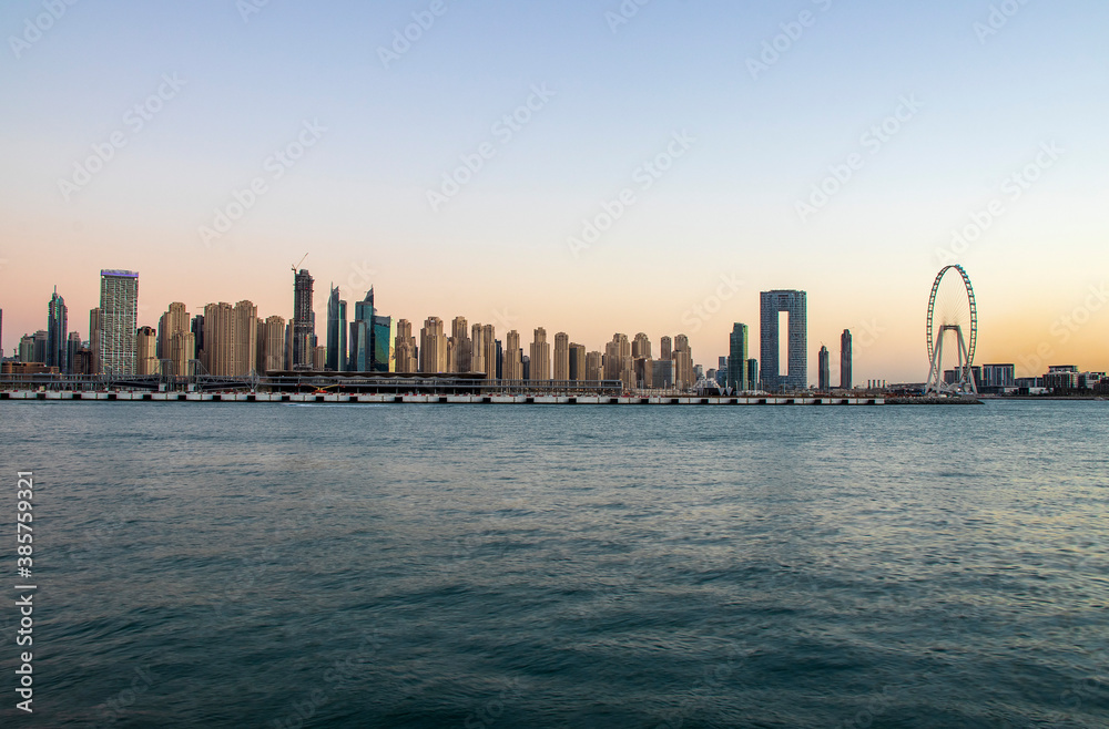 View of A Jumeirah Beach Residence and Blue waters during sunset hour. Shot made from Palm Jumeirah, man made island. Tallest ferris wheel, Ain Dubai can also be seen in the scene Dubai, UAE. View of A Jumeirah Beach Residence and Blue waters during sunset hour. Shot made from Palm Jumeirah, man made island. Tallest ferris wheel, Ain Dubai can also be seen in the scene Dubai, UAE.