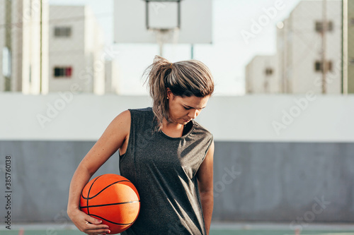 Young latin woman in sportswear playing basketball on outdoor court