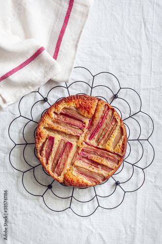 Top down view of a rhubarb and custard pie on round cooling rack on white background