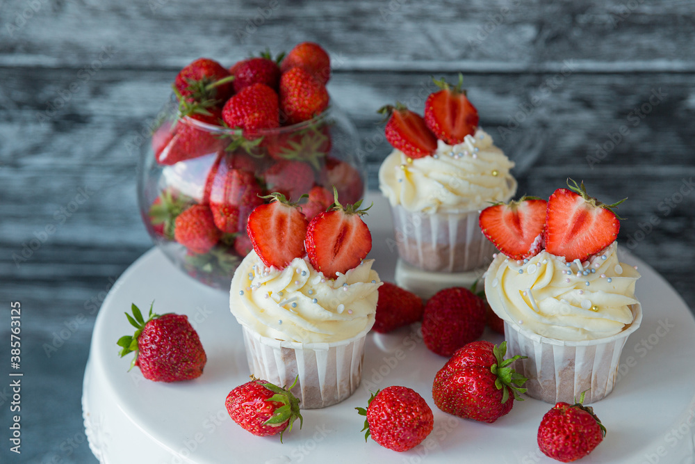 cupcake in the center with white cream decorated with ripe strawberries on a gray blue background and scattered strawberries. cupcake in the center with white cream decorated with ripe strawberries on a gray blue background and scattered strawberries.