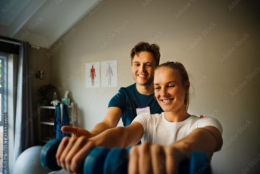 Male physiotherapist observing female patient holing weights Male physiotherapist observing female patient holing weights