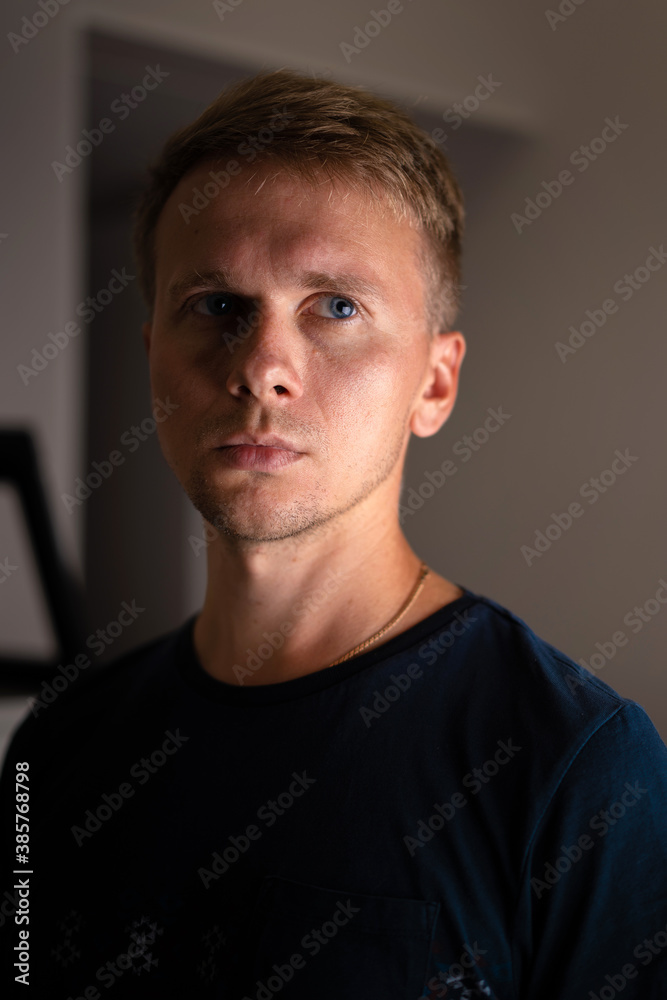 Obraz premium Portrait of a young blond man in a dark room with shadows