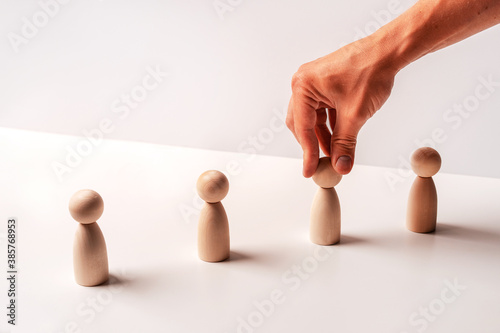 Wooden figures on a white background stand in a row and their male hand moves. The concept of subordination and management, copy space photo