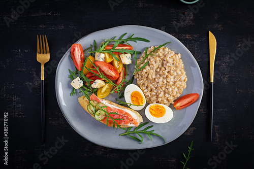 Breakfast oatmeal porridge with boiled egg, salmon sandwich and tomatoes salad. Healthy food. Top view, overhead, copy space