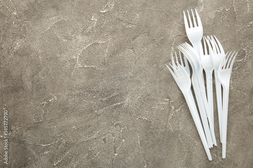 Many plastic forks on a grey concrete background.